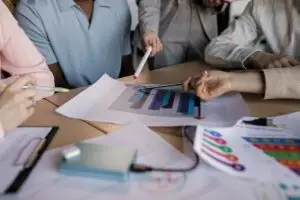 close-up on some documents showing some charts. Several professionals are sitting around the documents and pointing at the charts.