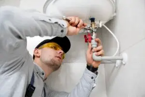 A plumber is using a tool to tighten the pipe fitting under a bathroom sink