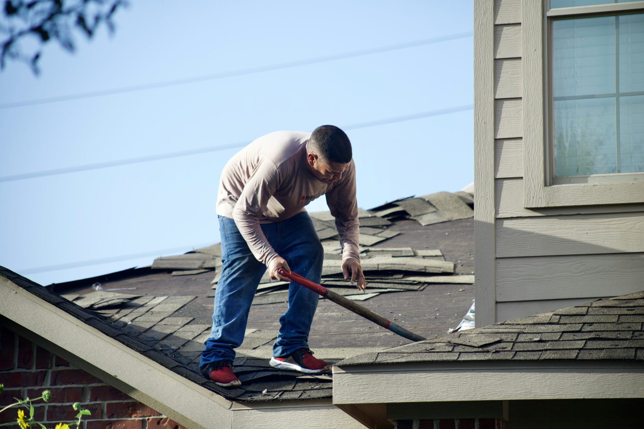 A roofer is on a residential roof removing old shingles
