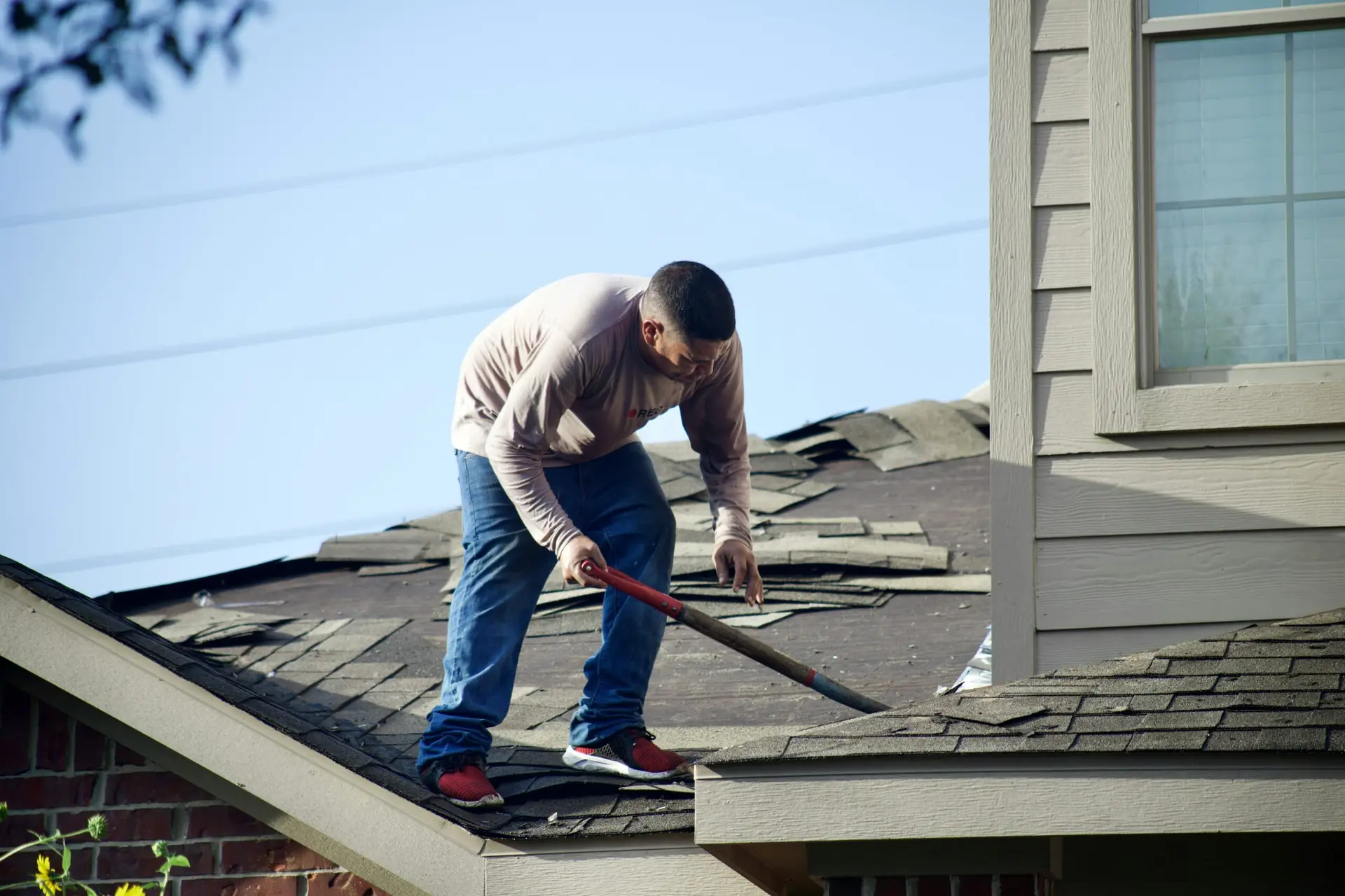 A roofer is on a residential roof removing old shingles